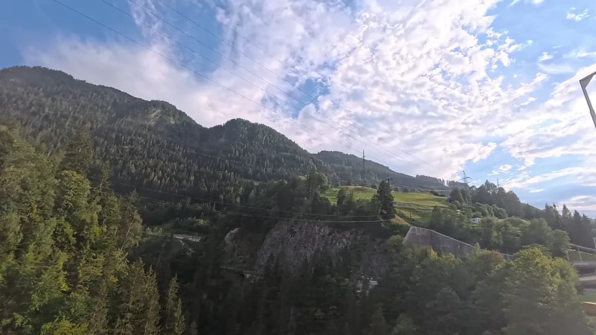 Blick von oben über bewaldete Hänge ins Tal, Stromleitungen, Schleierwolken