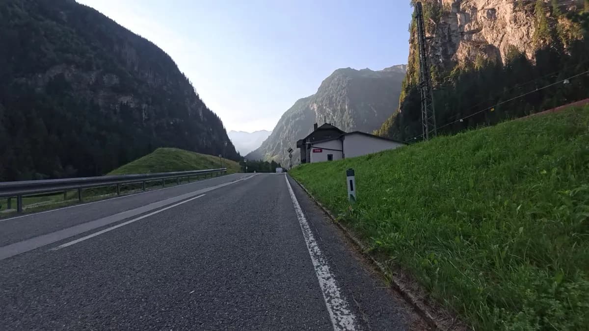 Leere Straße am Morgen zwischen Felswänden, rechts ein kleines Bahngebäude