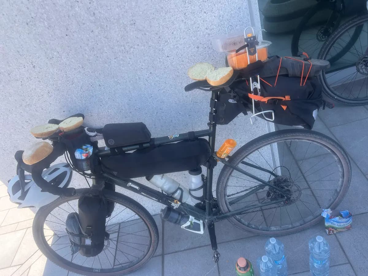 Bepacktes Gravelbike an einer Hauswand, Brötchen auf Lenker und Sattel, Wasserflaschen auf dem Boden