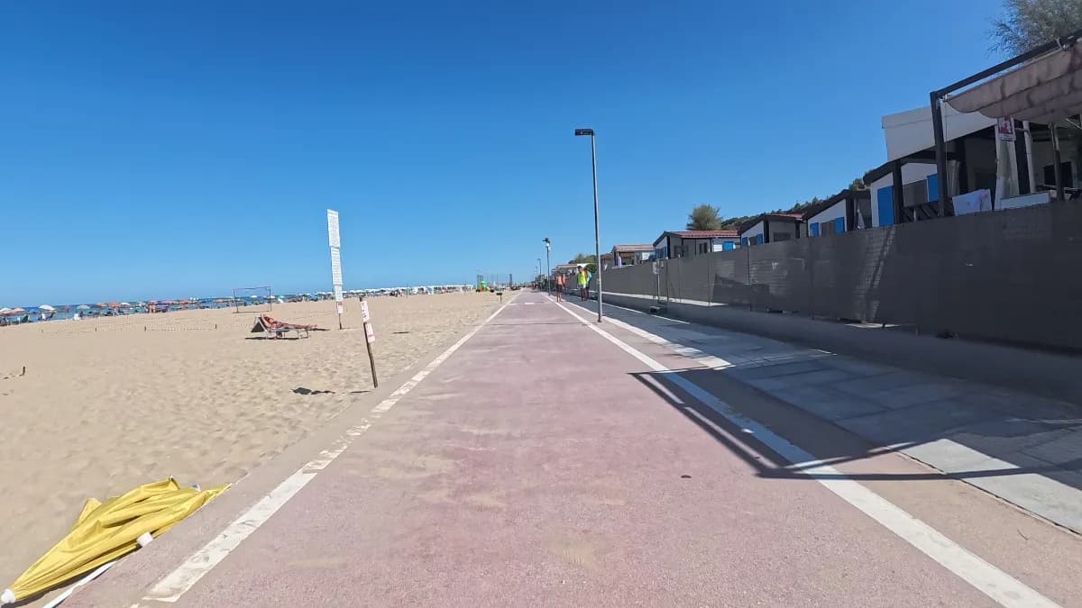 Roter Radweg an einem Sandstrand, daneben Strandbäder und Sonnenschirme