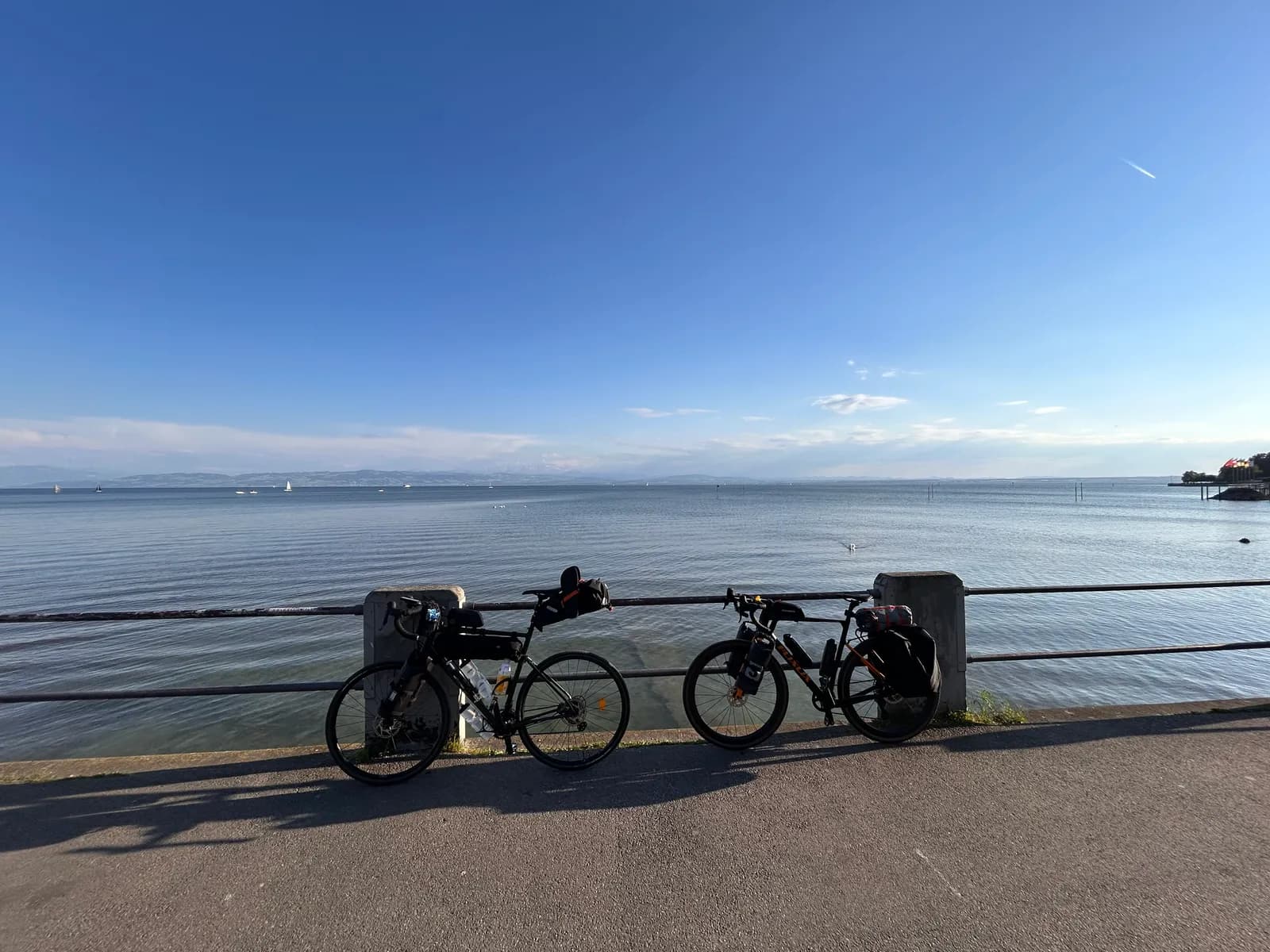 Zwei bepackte Räder mit Rennlenker an einem Geländer am Bodensee, links mit Sattel- und Rahmentasche, rechts mit Gepäckträger und Packtaschen, 2025.